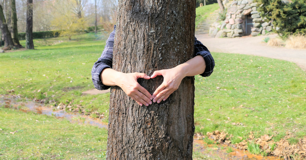 Frau umarmt Baum und formt mit ihren Händen ein Herz